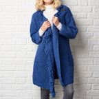 Person wearing a blue crochet cardigan against a white brick wall