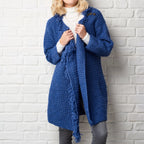 Person wearing a blue knitted cardigan against a white brick wall