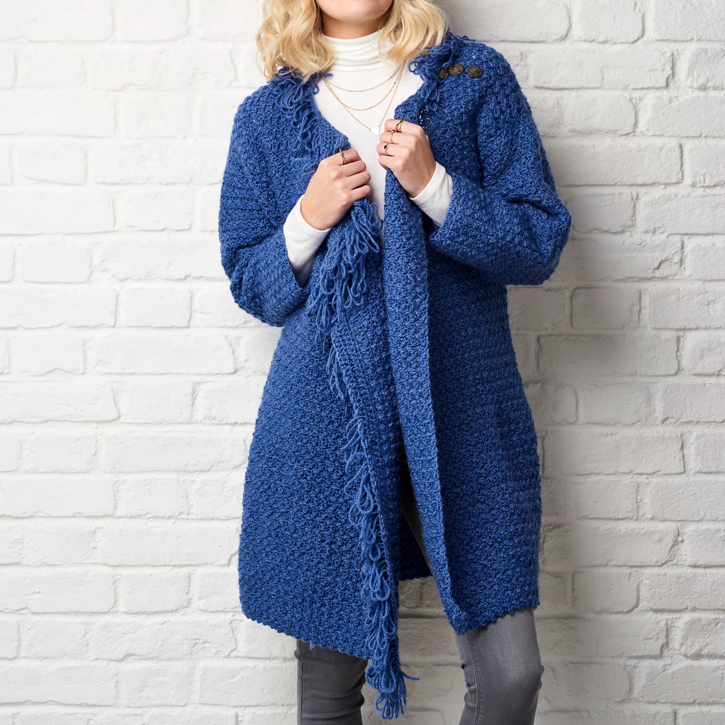 Person wearing a blue knitted cardigan against a white brick wall
