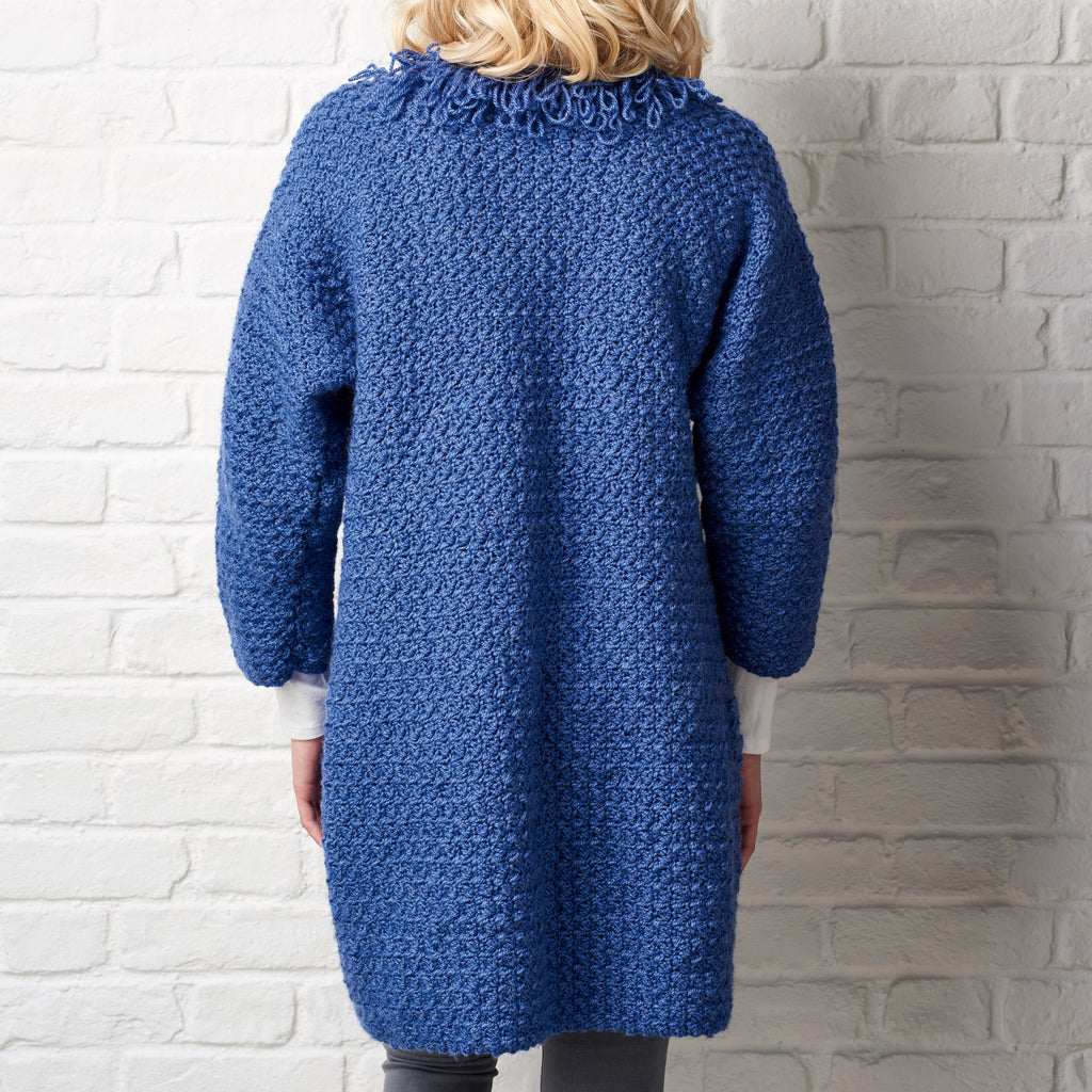 Person wearing a blue crochet cardigan against a white brick wall.