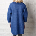 Person wearing a blue crochet cardigan against a white brick wall.