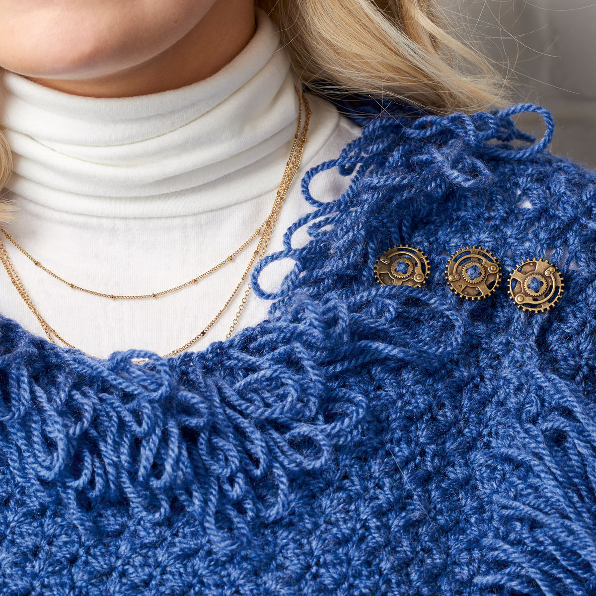 Close-up of a person wearing a blue crochet garment with gold jewelry.