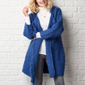 Woman wearing a blue crochet cardigan against a white brick wall