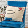 Crocheted letter-shaped pillow with heart and 'By Airmail' text on a blue chair.
