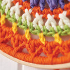 Close-up of a crochet mandala hoop featuring a series of colorful stitches in orange, green, white, and yellow shades.