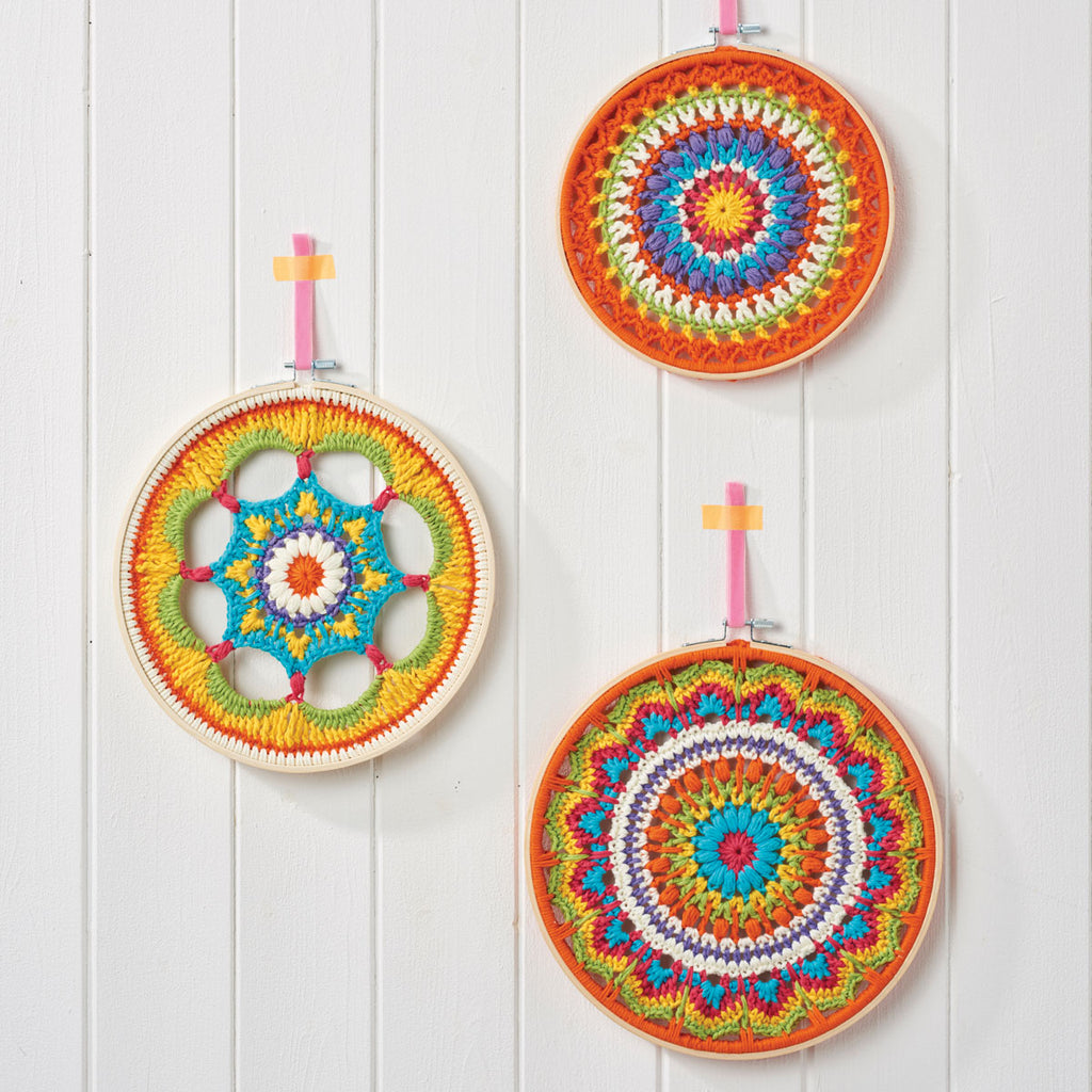 A set of three colorful mandala-style crochet hoops displayed against a white wooden background.