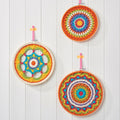 A set of three colorful mandala-style crochet hoops displayed against a white wooden background.