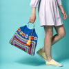 Person holding a colorful crochet bag against a turquoise background