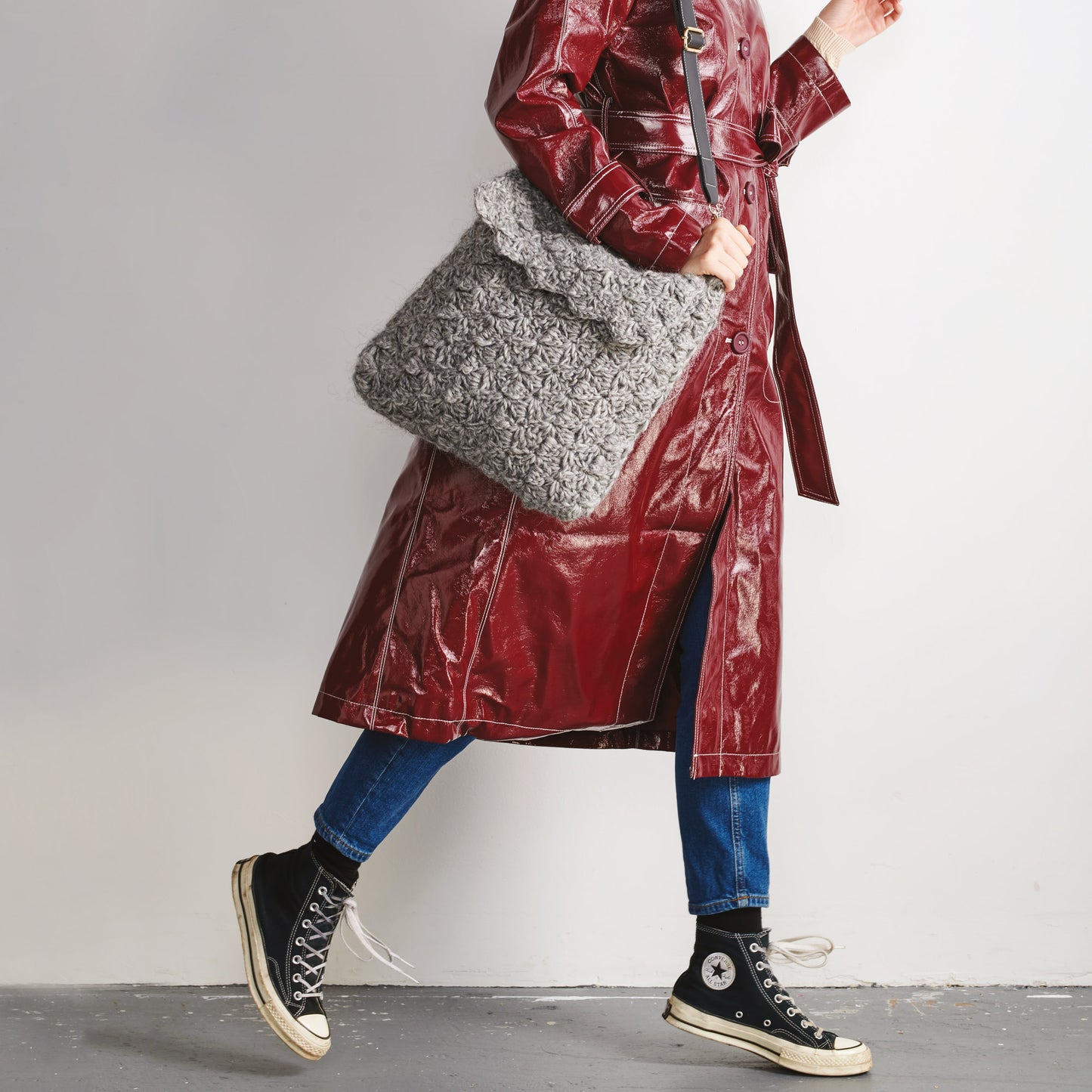 Person wearing a red raincoat holding a gray textured bag on a plain background