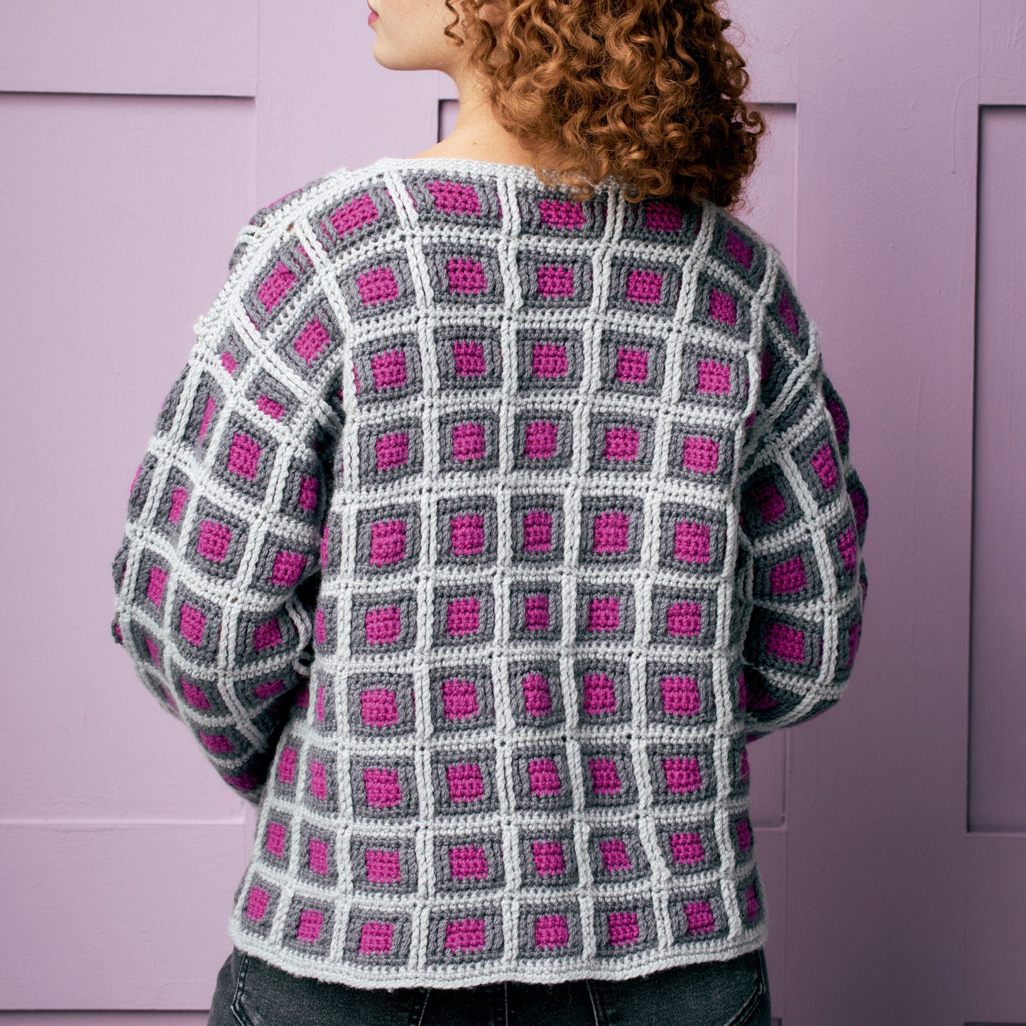 Person wearing a crocheted sweater with a grid pattern against a purple background