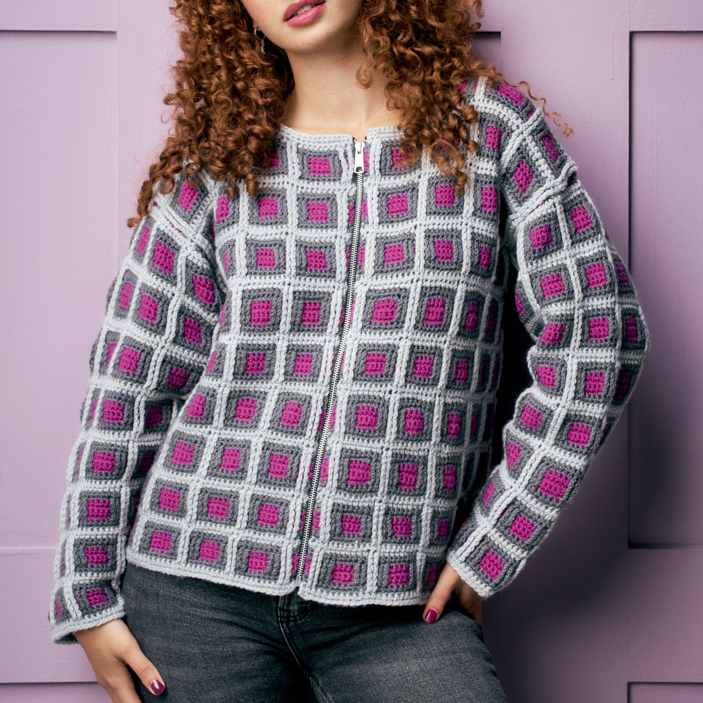 Person wearing a crocheted jacket with a grid pattern against a pink background