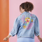 Person wearing a denim jacket with floral designs on a two-tone background