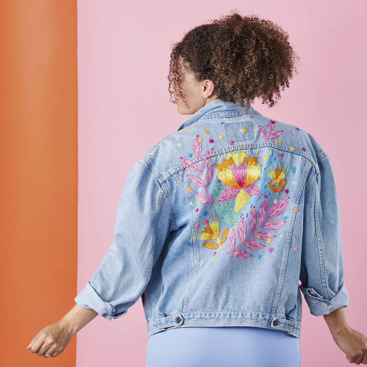 Person wearing a denim jacket with floral designs on a two-tone background
