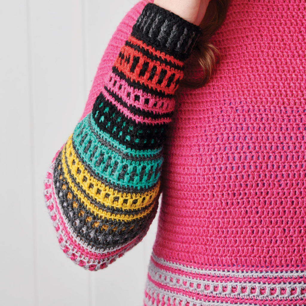 Person wearing a vibrant crochet sweater with a hot pink body and colorful striped sleeve in black, orange, pink, teal, and yellow patterns.