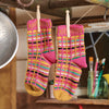 Colorful crochet socks hanging on a line with kitchen utensils in the background.