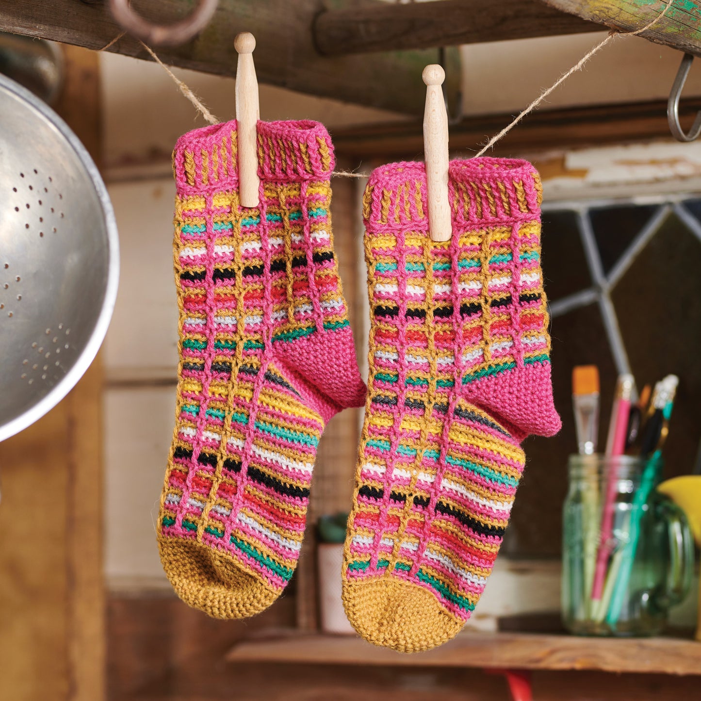 Colorful crochet socks hanging on a line with kitchen utensils in the background.