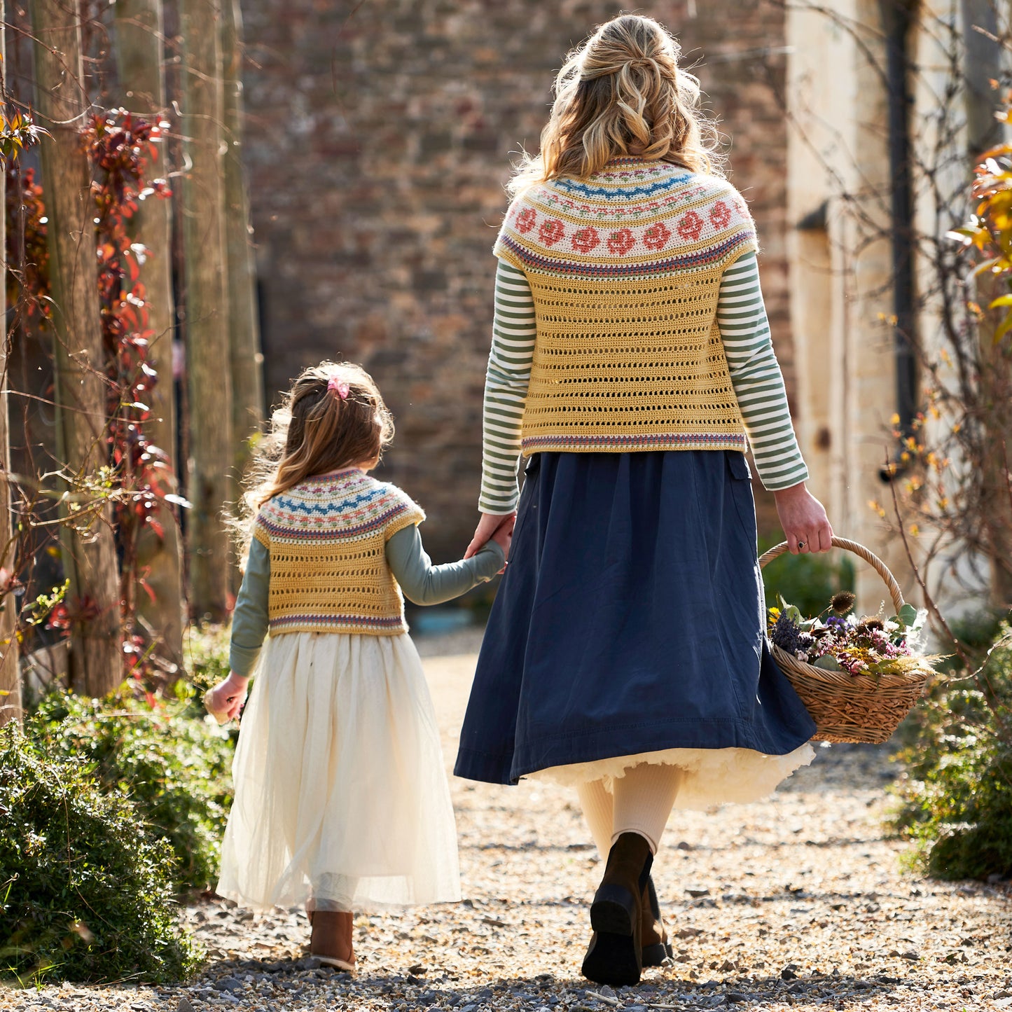 Two people walking together in a garden, both wearing patterned cardigans.