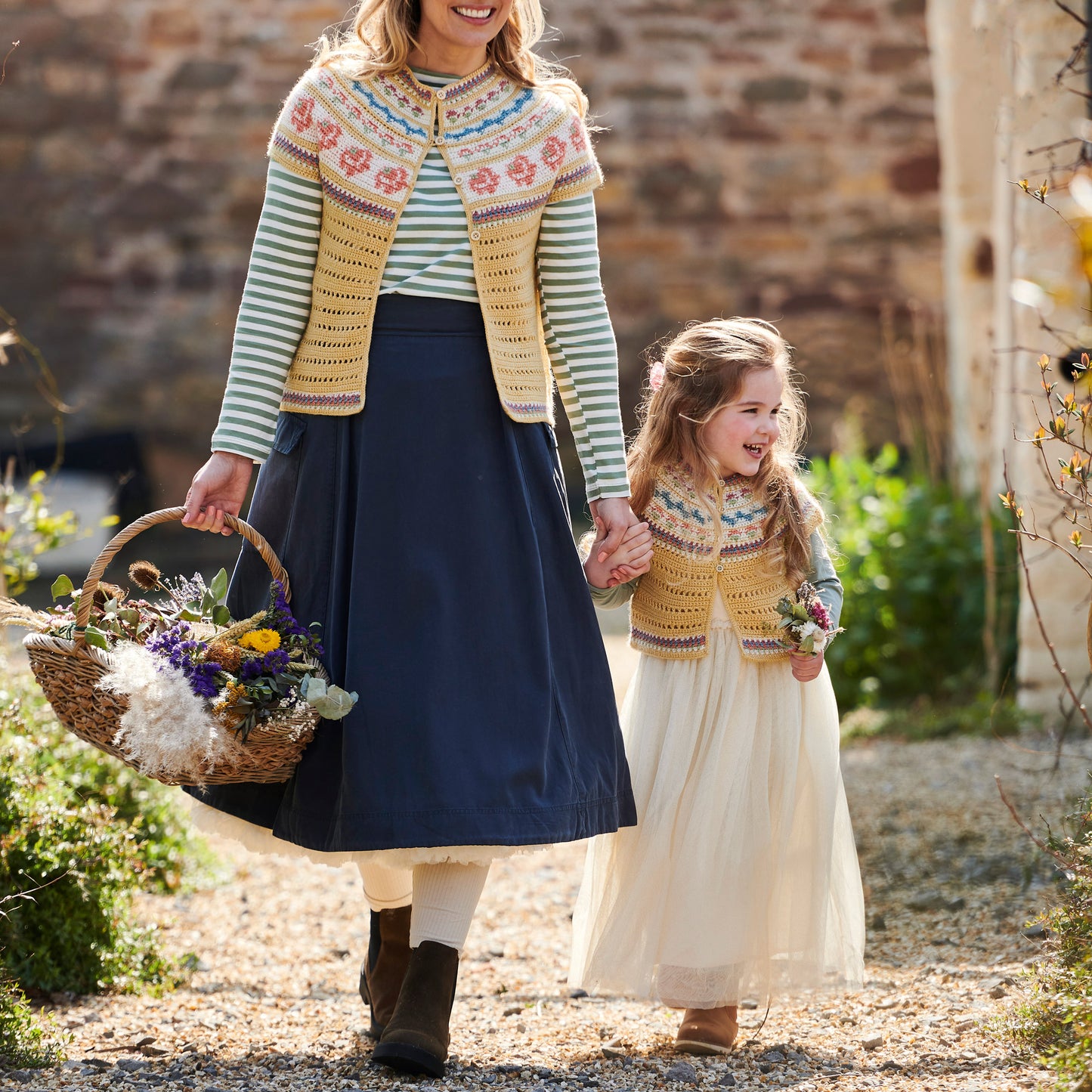 Woman and young girl walking outdoors holding hands, both wearing crochet tops.
