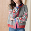 Person wearing a gray crochet cardigan with colorful floral patterns against a wooden background