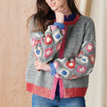 Person wearing a gray crochet cardigan with colorful floral patterns against a wooden background