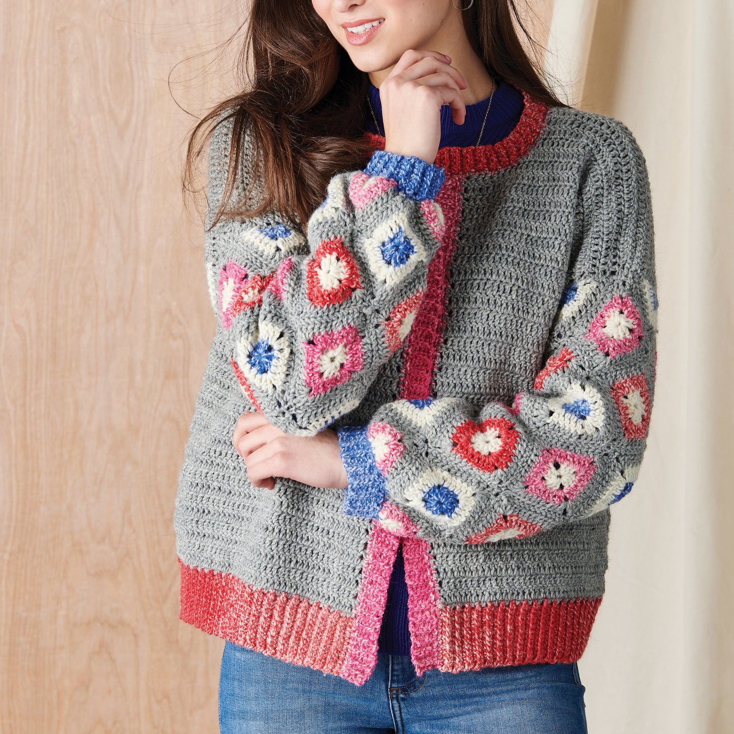 Person wearing a gray crochet cardigan with colorful floral patterns against a wooden background