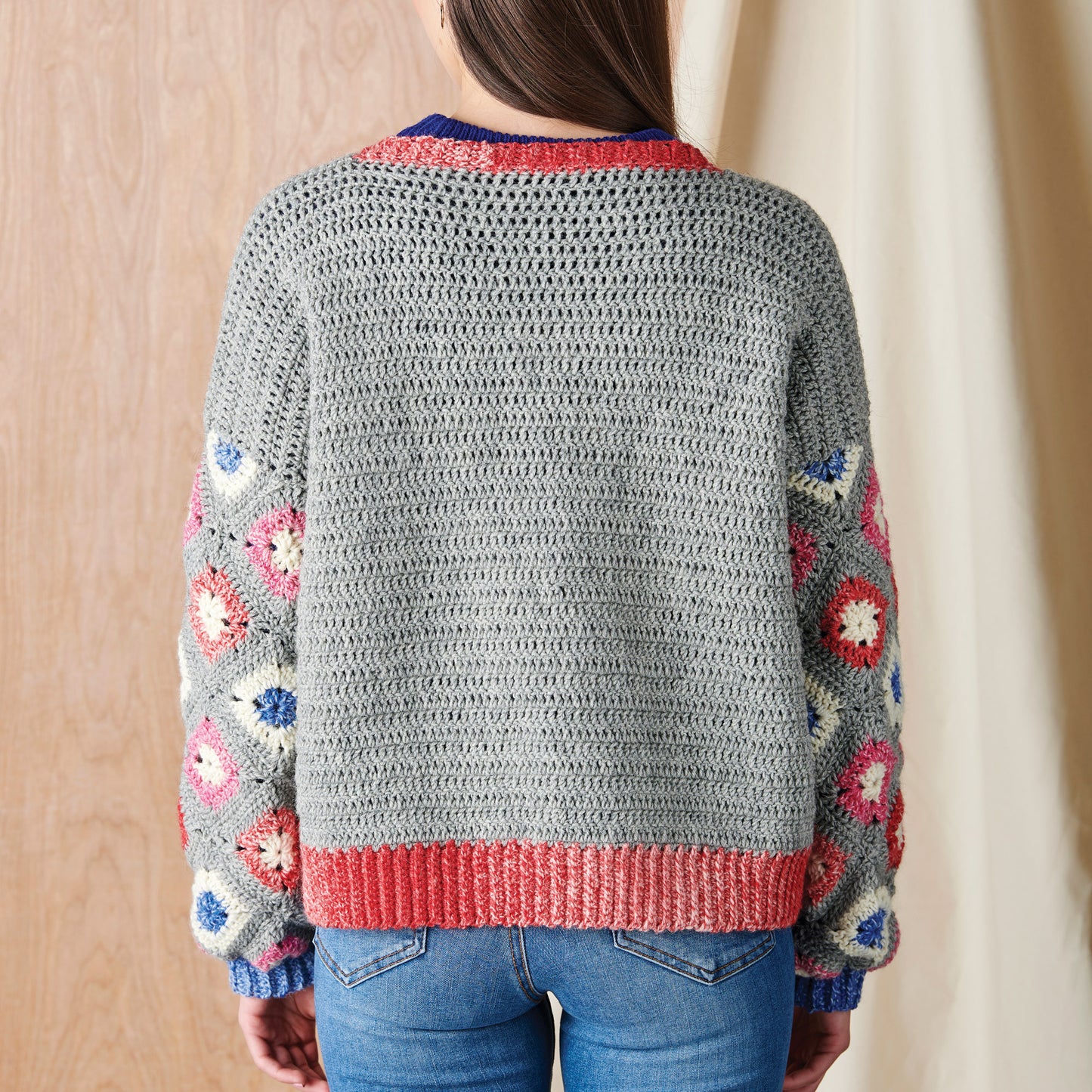 Person wearing a gray crochet sweater with colorful flower patterns against a neutral background