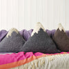 A series of mountain-shaped cushions in various colors with a textured crochet pattern, arranged on a bed with a pink blanket.