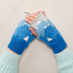 A pair of knitted wristwarmers with a mountain and patchwork pattern in blue and white colors, being worn by a person.
