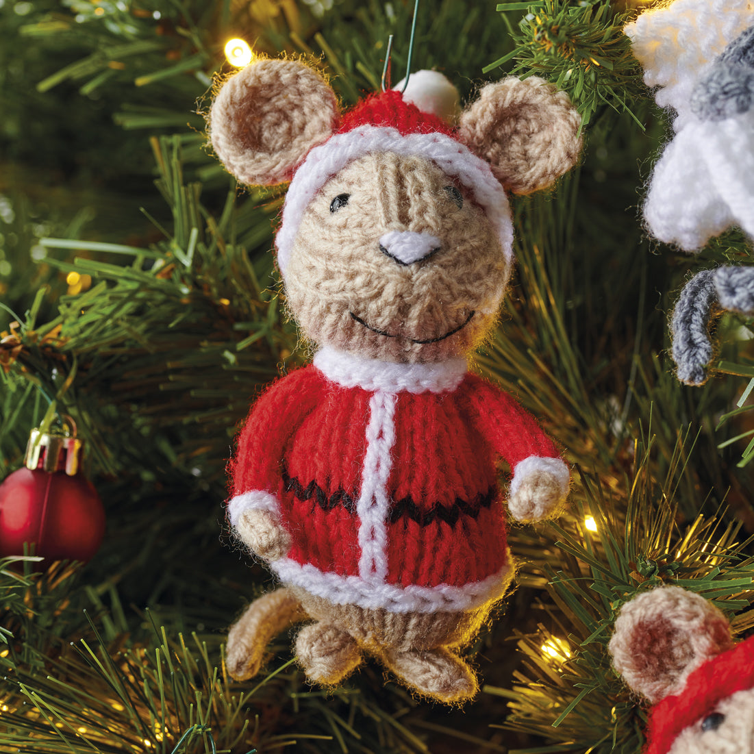 Knitted mouse ornament in a red sweater and Santa hat on a Christmas tree.