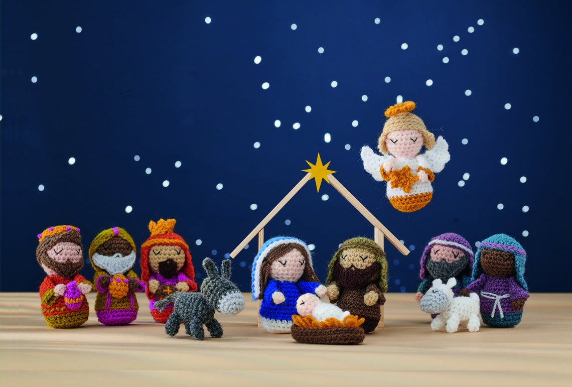 Crocheted nativity scene with figures of Mary, Joseph, and baby Jesus under a star, surrounded by wise men, an angel, sheep, and a donkey on a wooden table.