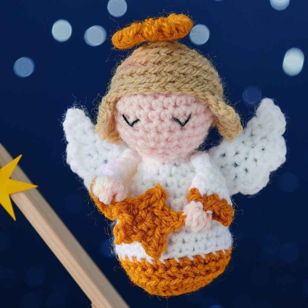 Crocheted angel ornament with closed eyes, white wings, and a golden halo against a starry blue background. The angel holds an orange star.