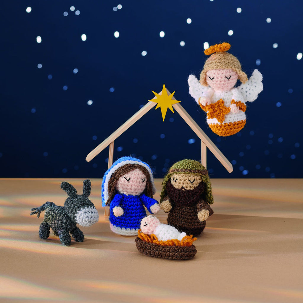 Crocheted nativity scene with an angel above, featuring Mary, Joseph, baby Jesus in a manger, a donkey, and a wooden stable under a starry night.