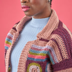 Person wearing a colorful crocheted cardigan against a pink background