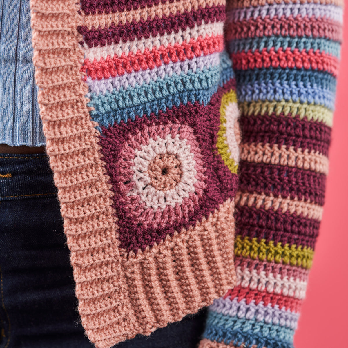 Colorful crocheted blanket with a square pattern on a pink background