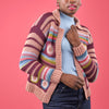 Person wearing a colorful striped crochet cardigan against a pink background