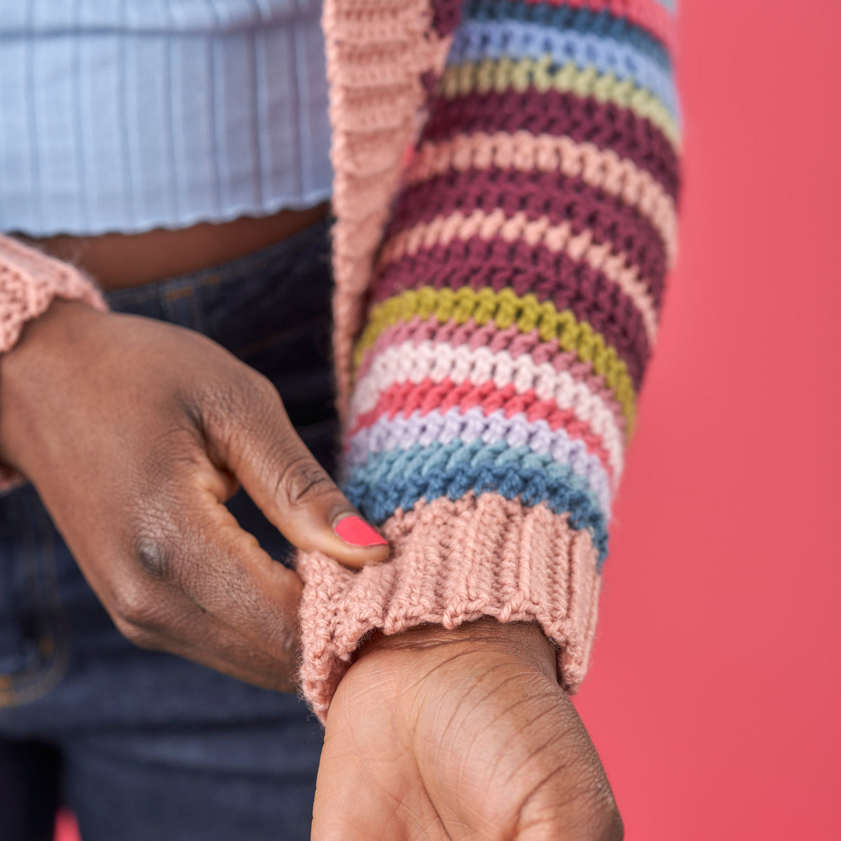 Close-up of a person wearing a colorful striped sweater with a pink cuff against a red background