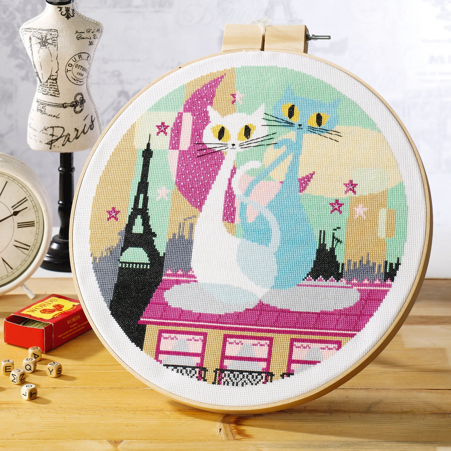 Cross-stitched hoop with a cat design featuring the Eiffel Tower on a wooden surface.