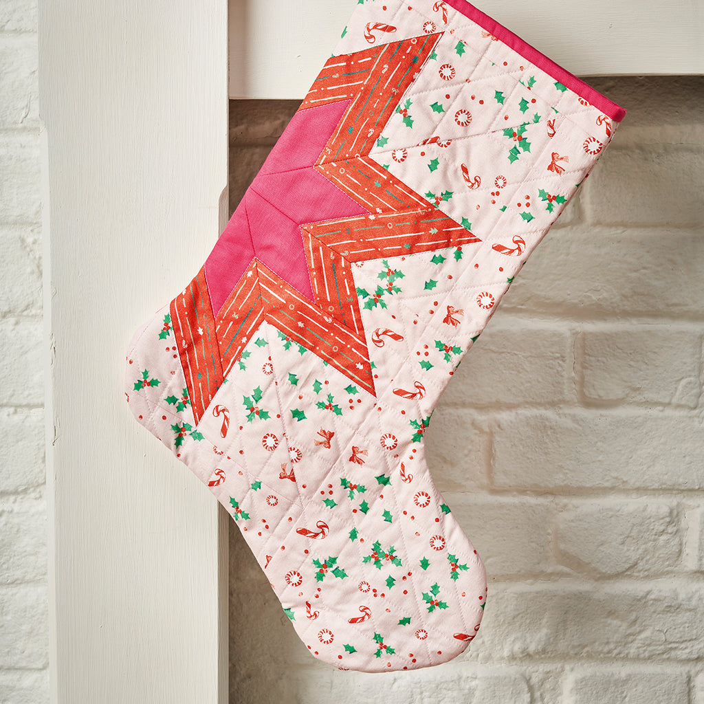Quilted Christmas stocking with geometric pattern on a white brick wall background