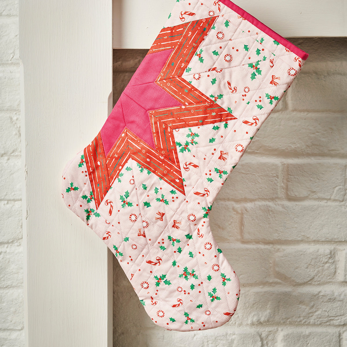 Quilted Christmas stocking with geometric pattern on a white brick wall background