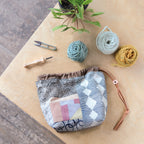 Fabric pouch with geometric pattern on a wooden surface with yarn and knitting tools.