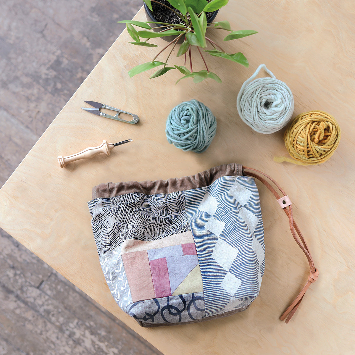 Fabric pouch with geometric pattern on a wooden surface with yarn and knitting tools.