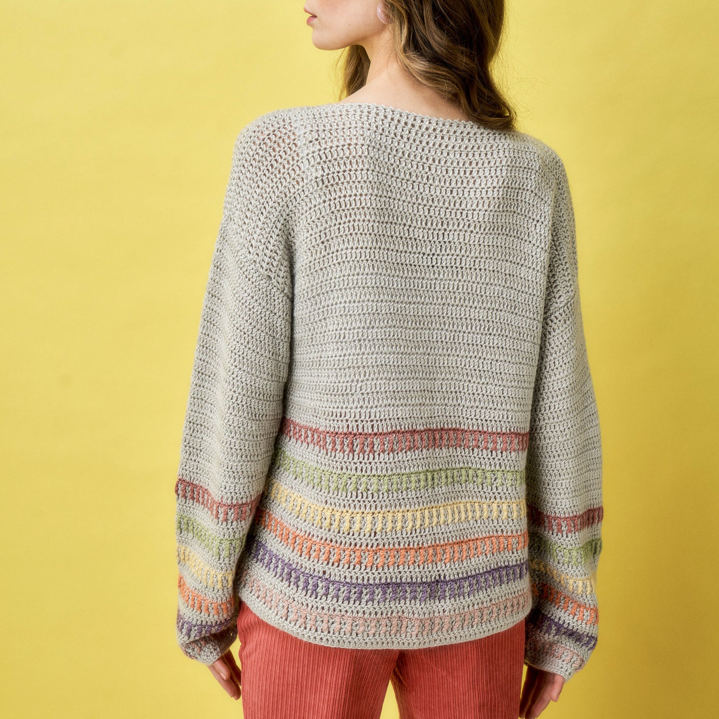 Person wearing a crocheted sweater with colorful stripes on a yellow background