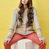 Woman wearing a colorful striped sweater and red pants against a yellow background
