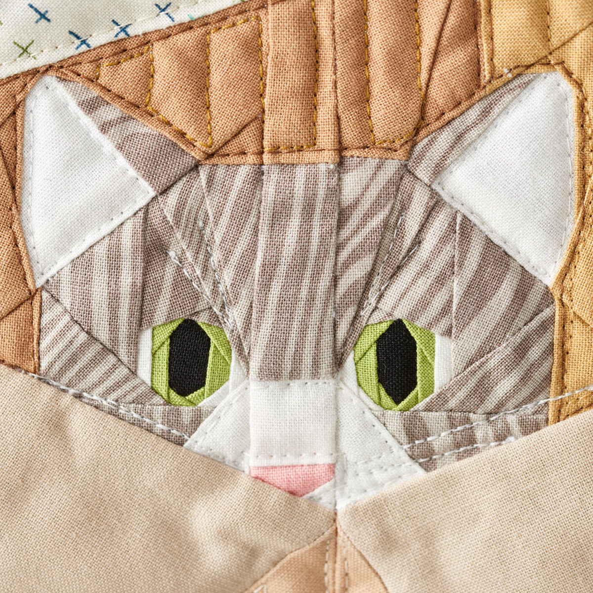 Quilted patchwork cat face with green eyes and a pink nose.