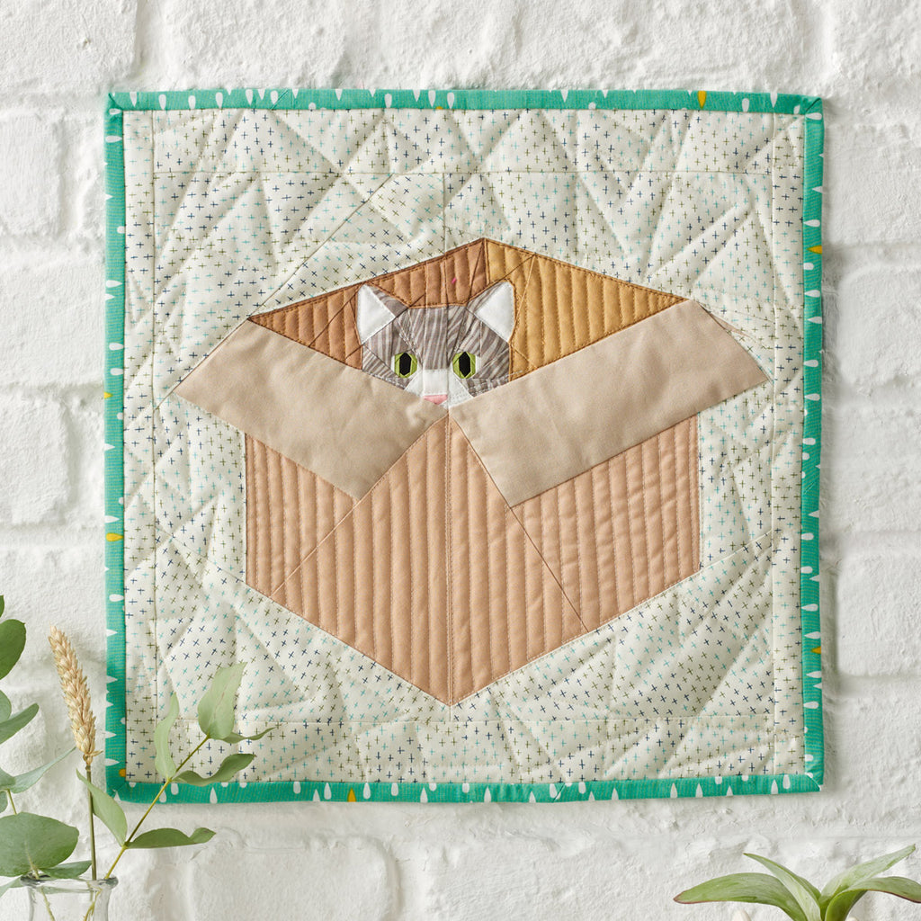 Quilted wall hanging with a cat design on a white background