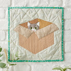 Quilted wall hanging with a cat design on a white background