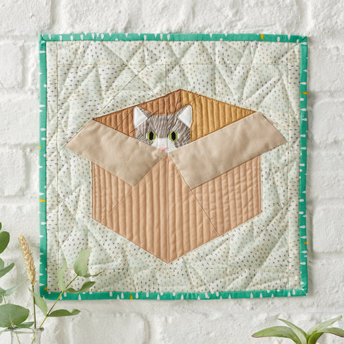 Quilted wall hanging with a cat design on a white background