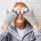 A person wearing gray knitted mittens with a penguin design on the cuffs.