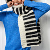 Person wearing a blue sweater and a black and white striped scarf against a white background
