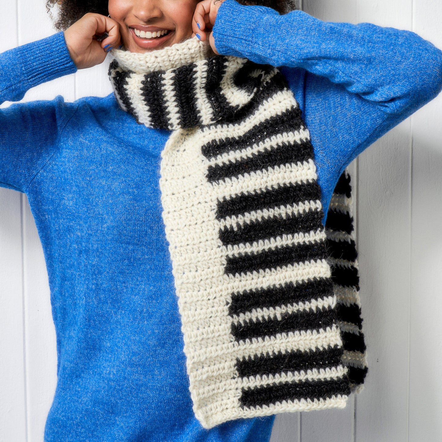 Person wearing a blue sweater and a black and white striped scarf against a white background